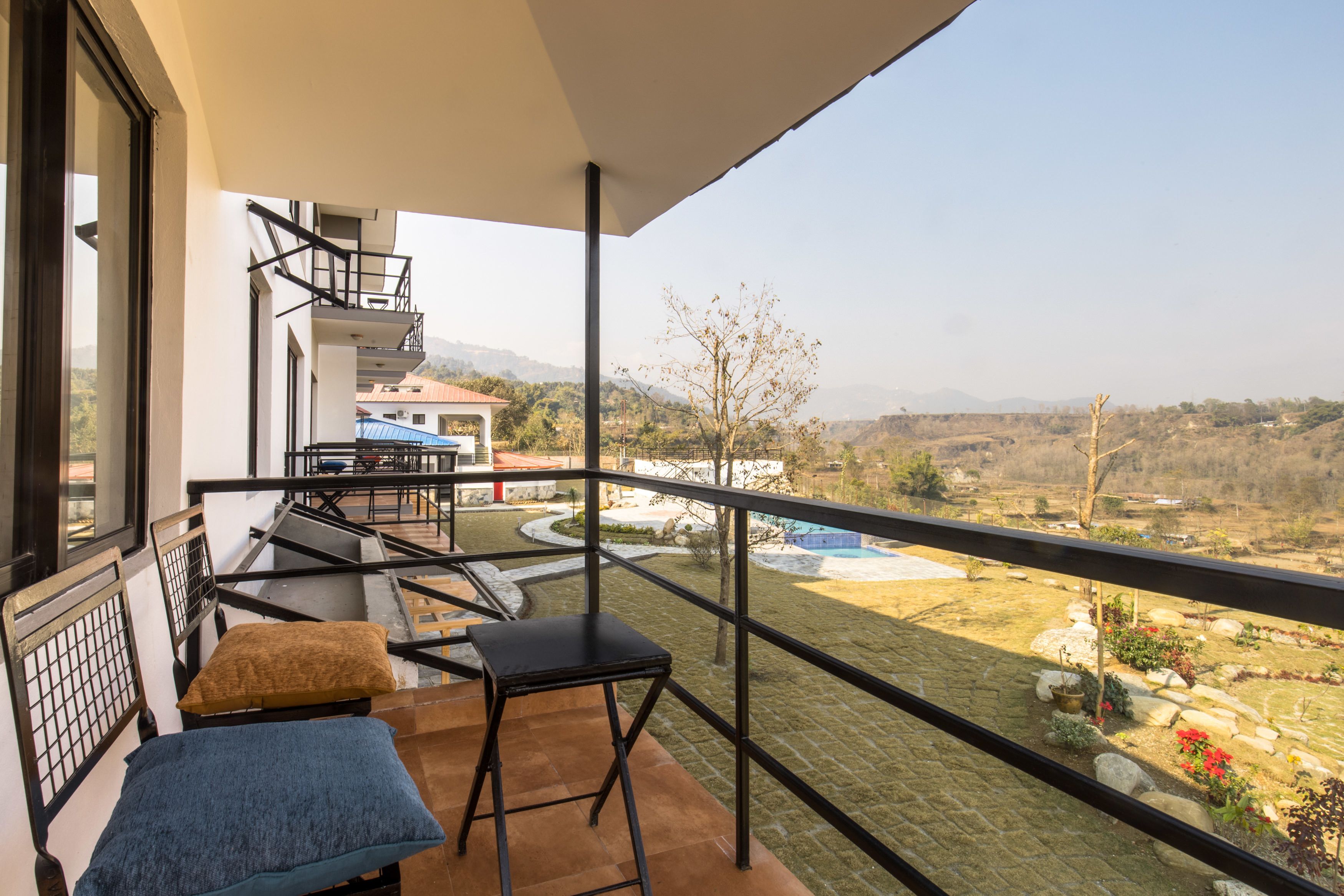 A balcony with a view of a pool and garden, a small table with a cushion, and a chair.