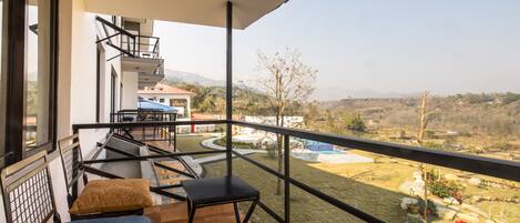 A balcony with a view of a pool and garden, a small table with a cushion, and a chair.