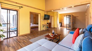 A spacious living area with a sofa, a coffee table with fruit, a TV, and a sliding door leading to a balcony.