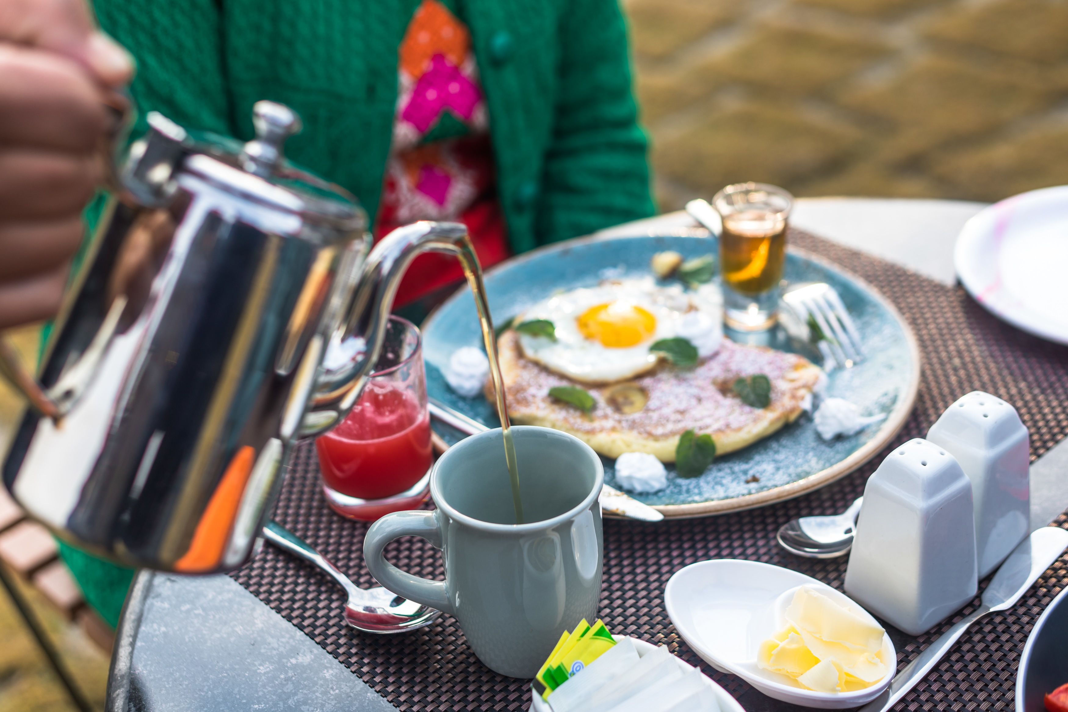 A breakfast setup with a coffee pot, mug, plate with eggs, and butter on a table.