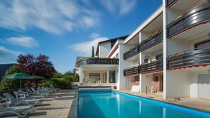 A swimming pool with lounge chairs and a building with balconies. - BSW - Schwarzwaldhotel Baiersbronn (Baiersbronn)