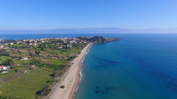 Vista aérea de un pueblo costero con playa, casas y montañas al fondo.