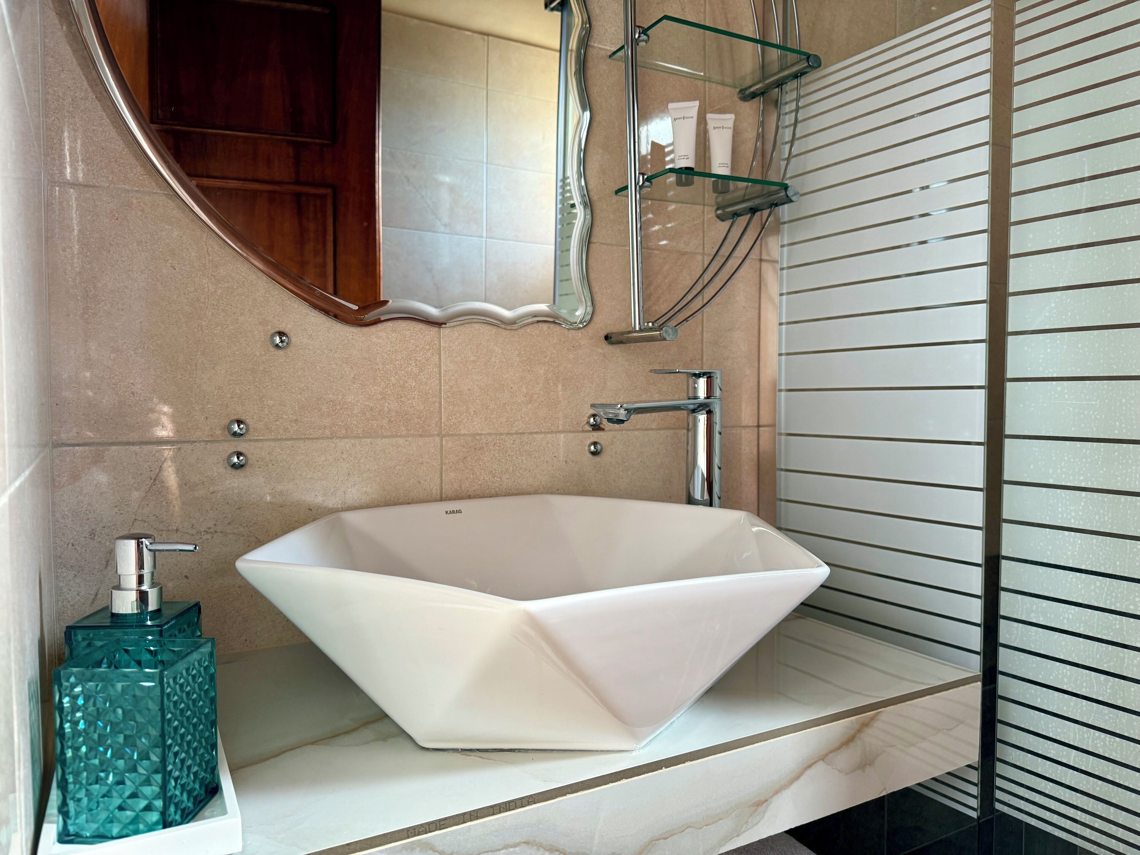 A modern bathroom with a white vessel sink, a glass shower enclosure, and a marble countertop.