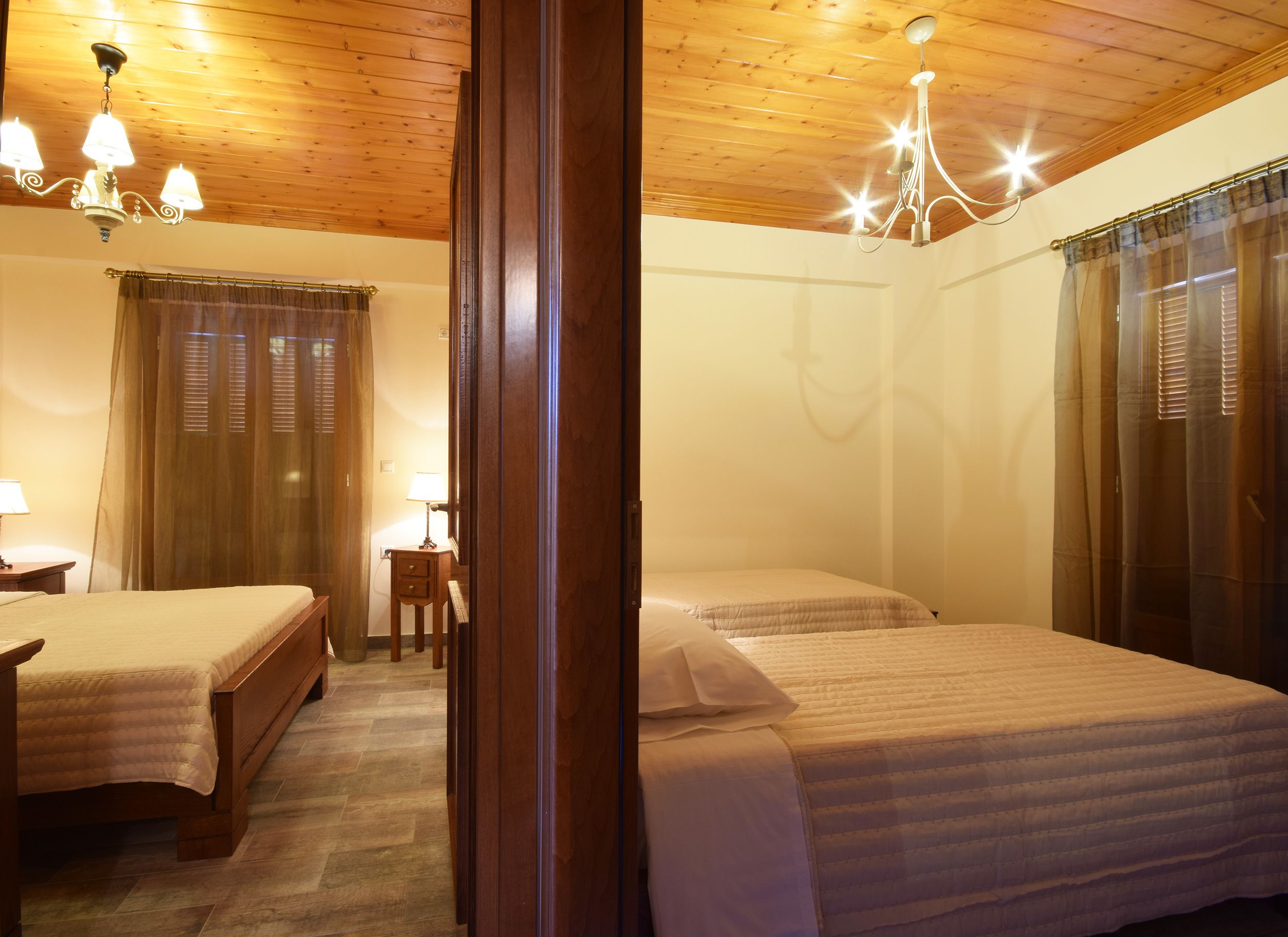 A room with two beds, wooden ceiling, and a chandelier.