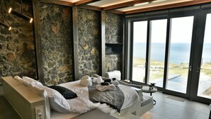 Une chambre moderne avec un mur en pierre, un lit avec des serviettes, une petite table et une vue sur la mer.