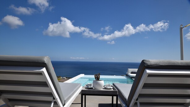 Un salon au bord de la piscine avec deux chaises longues, une table agrémentée d’une plante en pot et une vue dégagée sur l’océan.