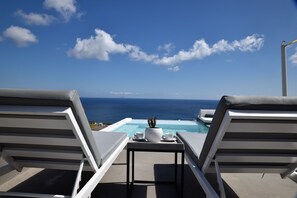A poolside lounge with two reclining chairs, a table with a potted plant, and a clear view of the ocean. - Horizon Mills Villas & Suites (Santorini)