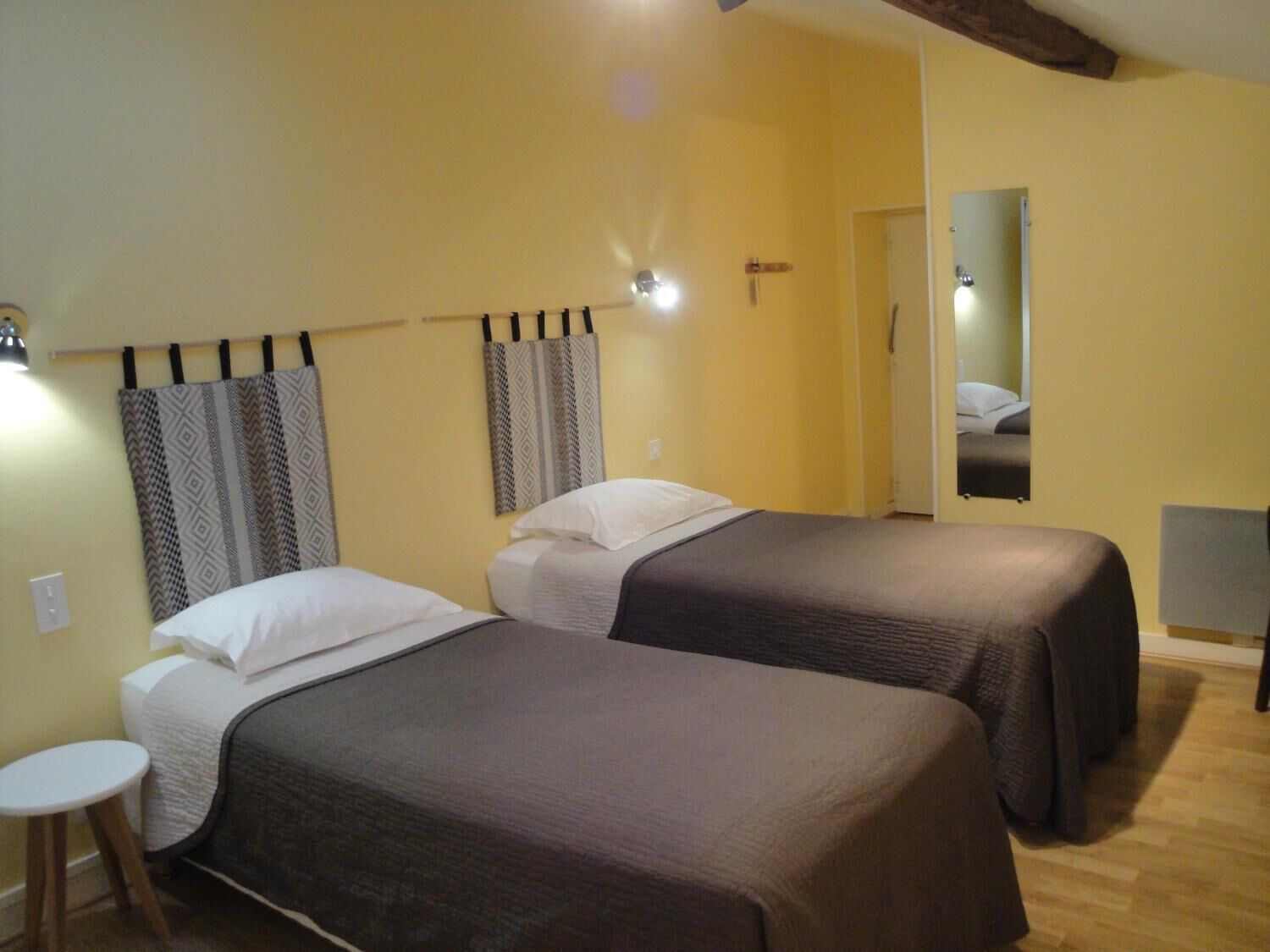 A room with two beds, a small table, and a mirror on the wall.