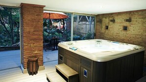 A spa area with a hot tub, wooden deck, and a view of a garden through large windows. - La Halte du Temps (Montesquieu-Volvestre)