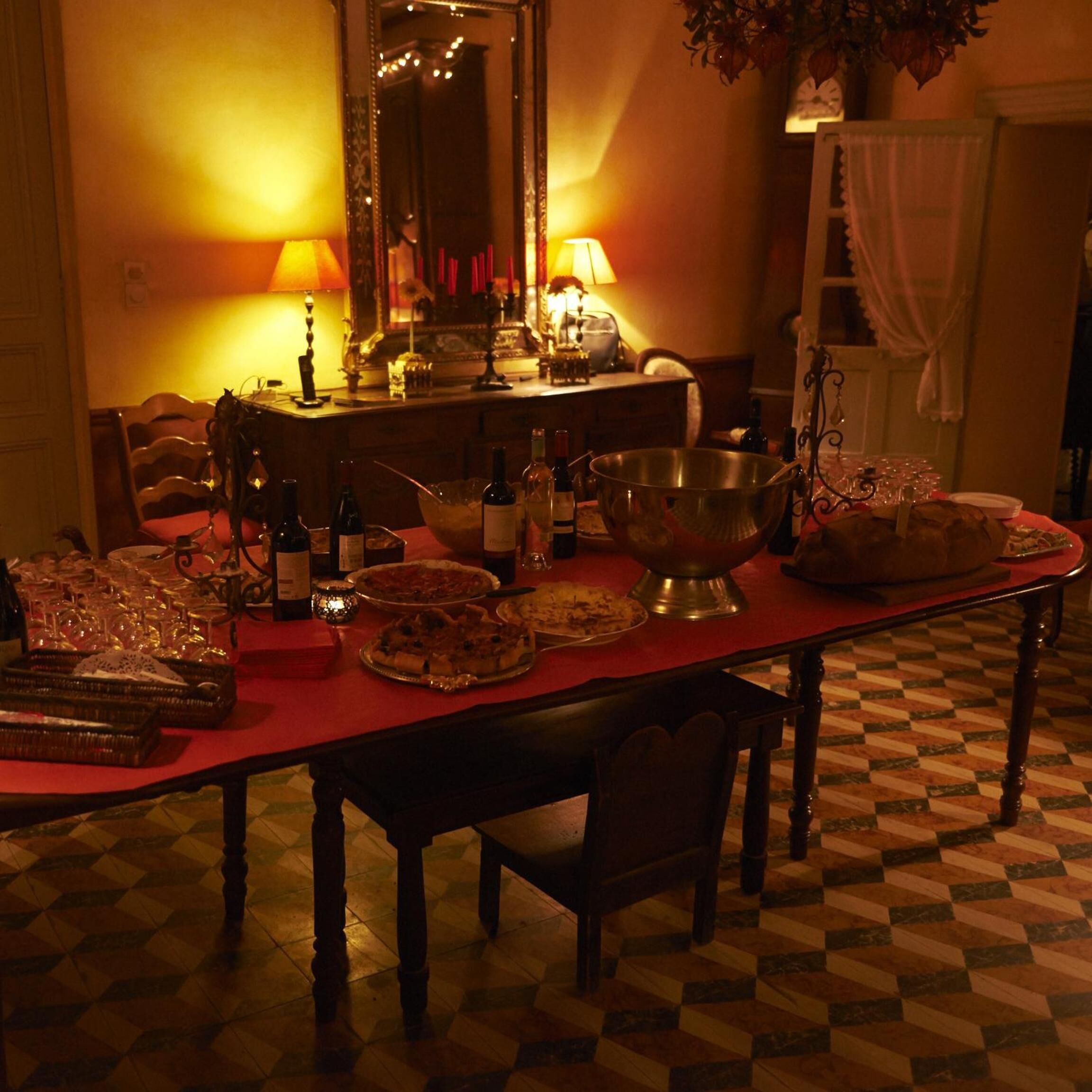 A dining area with a checkered floor, wooden chairs, a table set with plates, glasses, and bottles.