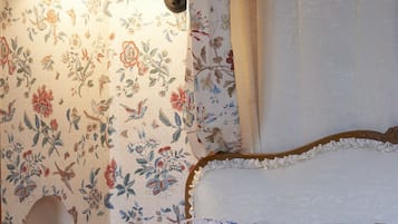 Un dormitorio con papel tapiz floral, una lámpara de noche, un cabecero de madera y una mesita de noche con un libro.