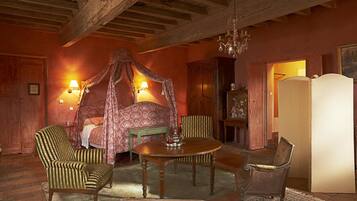 Een slaapkamer met een hemelbed, twee fauteuils, een houten tafel en een kroonluchter.