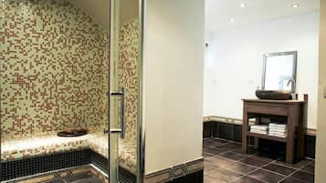 Une salle de bain avec un mur recouvert de mosaïques, une cabine de douche en verre, un meuble-lavabo en bois avec un miroir et un sol carrelé.