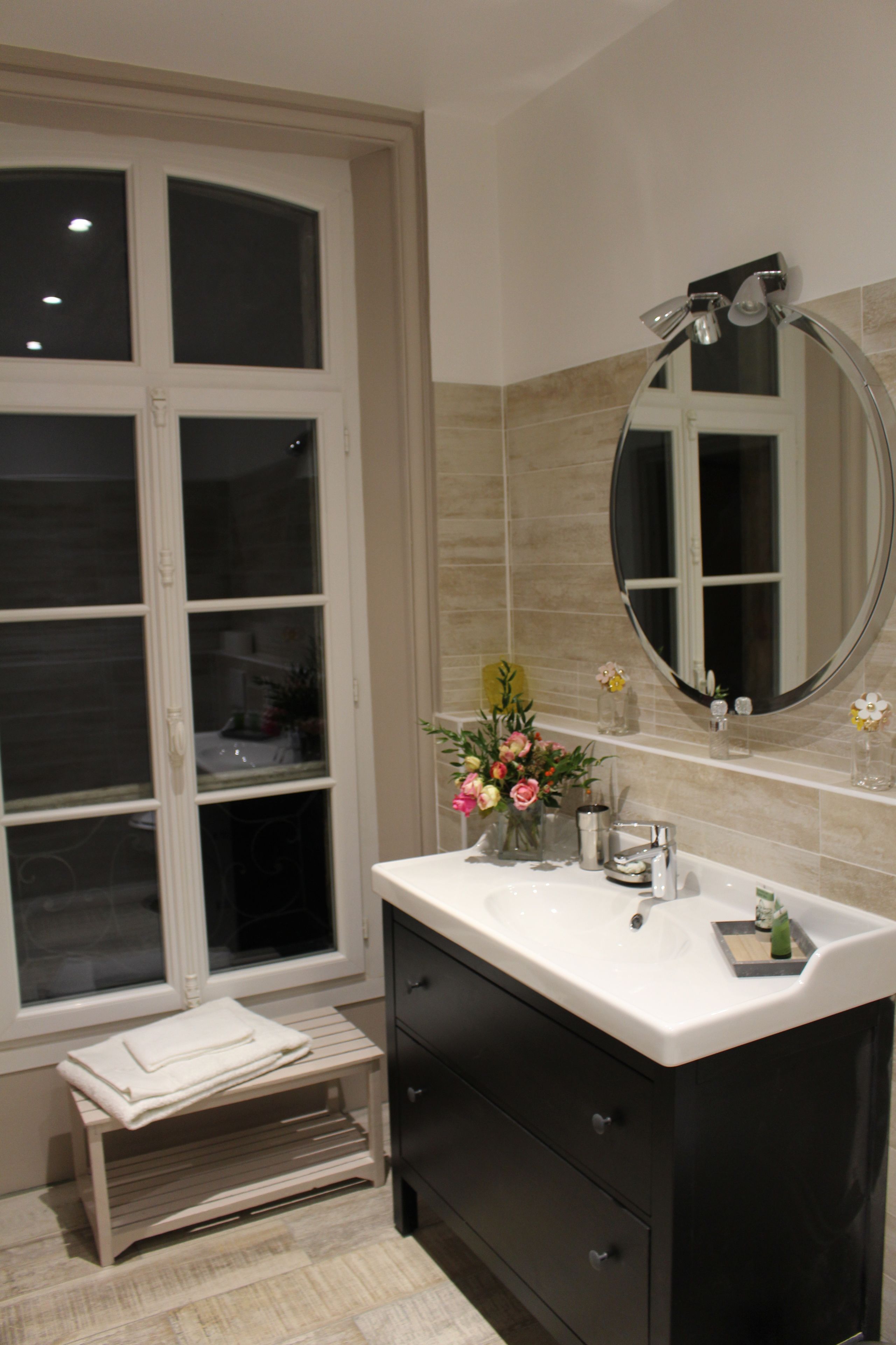 A bathroom with a large window, a sink with a mirror, and a small step leading to a shelf with toiletries.