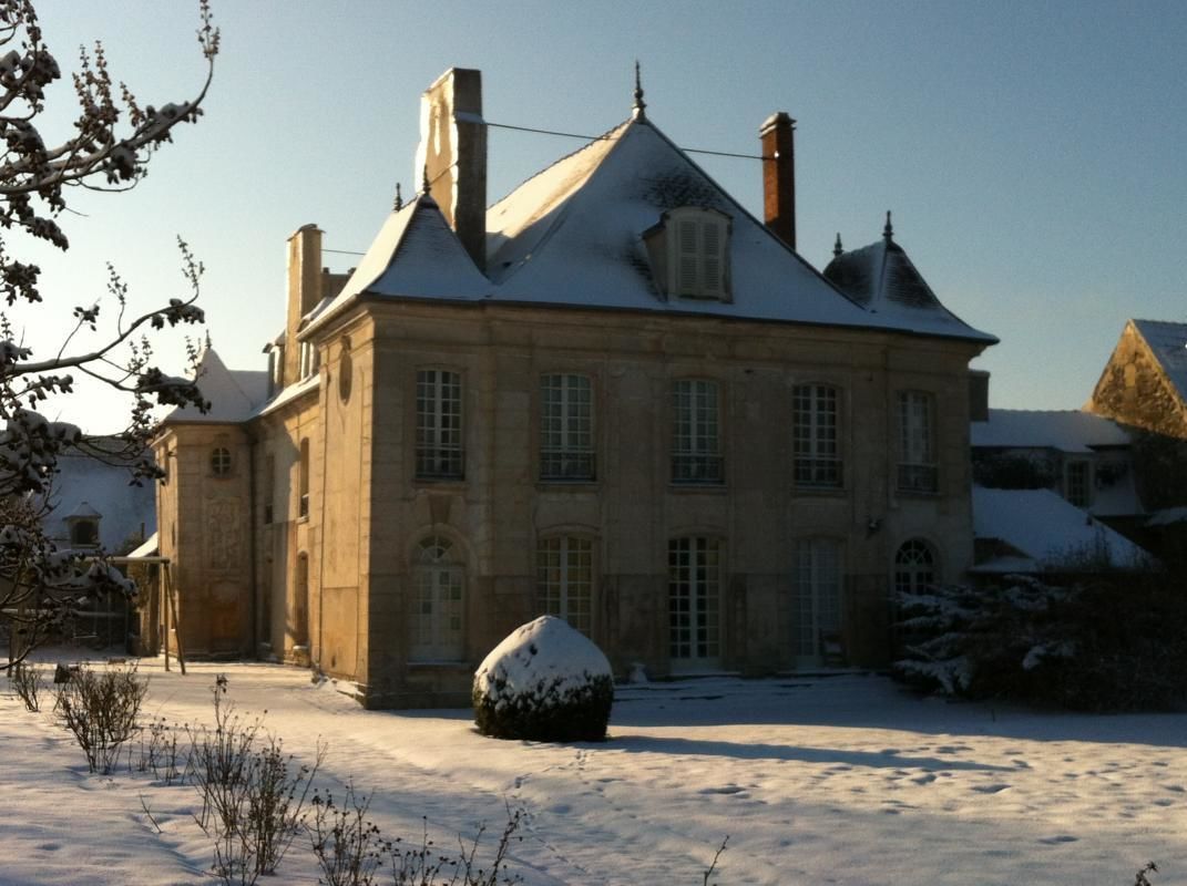 Un edificio grande e histórico con fachada simétrica, múltiples chimeneas y tejado cubierto de nieve.