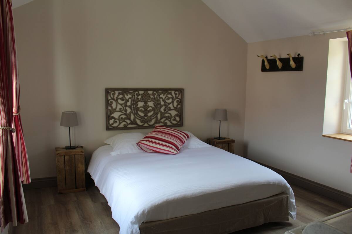 A bedroom with a large bed, two bedside tables, a decorative headboard, and a window with curtains.