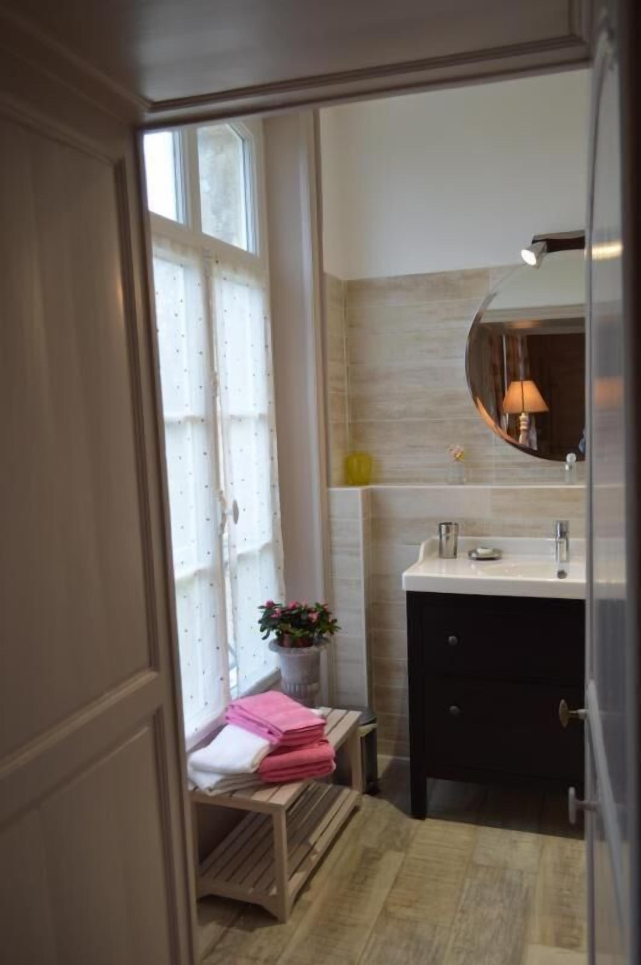 Ein Badezimmer mit weißem Waschtisch, einem Spiegel und einem Fenster mit Vorhängen.
