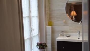 Ein Badezimmer mit weißem Waschtisch, einem Spiegel und einem Fenster mit Vorhängen.