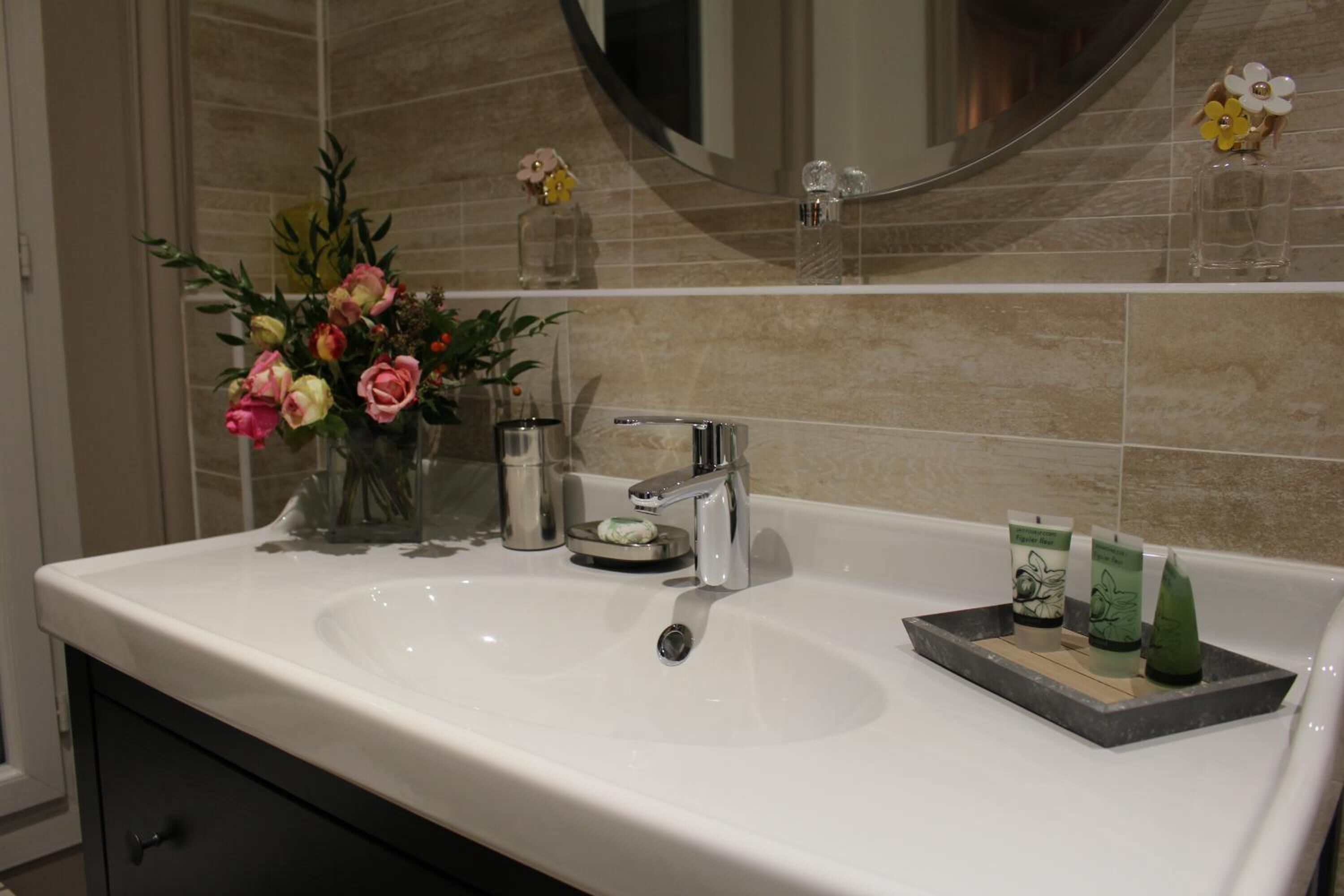 Un baño con un lavamanos blanco, un espejo y un florero con flores.