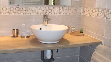 A bathroom with a white sink, mirror, and tiled walls. There are towels on the counter and a trash can below.