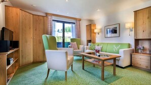 Ein gemütliches Wohnzimmer mit einem grünen Sofa, zwei Sesseln, einem Couchtisch und Holzschränken.