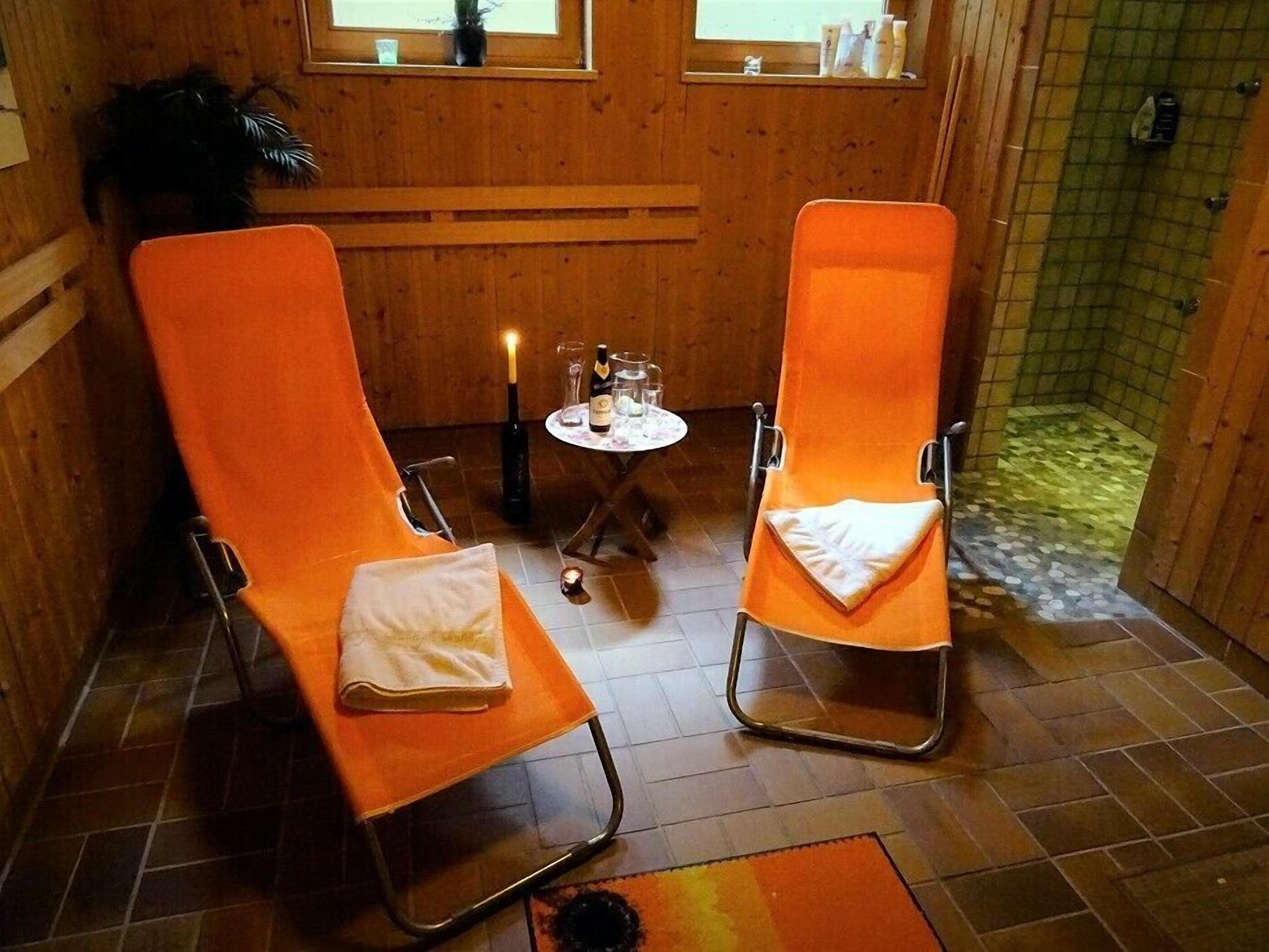 Une pièce avec deux fauteuils orange, une petite table sur laquelle se trouvent une bouteille et des verres, une bougie et un sol carrelé.