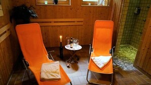 Ein Zimmer mit zwei orangenen Sesseln, einem kleinen Tisch mit Flasche und Gläsern, einer Kerze und einem Fliesenboden.