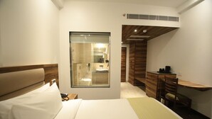 A hotel room with a bed, a desk, and a bathroom visible through a glass partition. - County Inn Hotel (Jaipur)