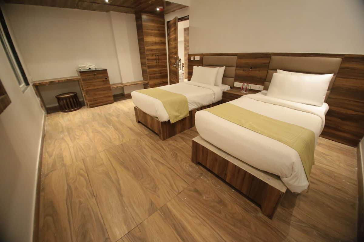 Habitación de hotel con dos camas, suelo de madera, un pequeño cubo de basura y un armario de madera.