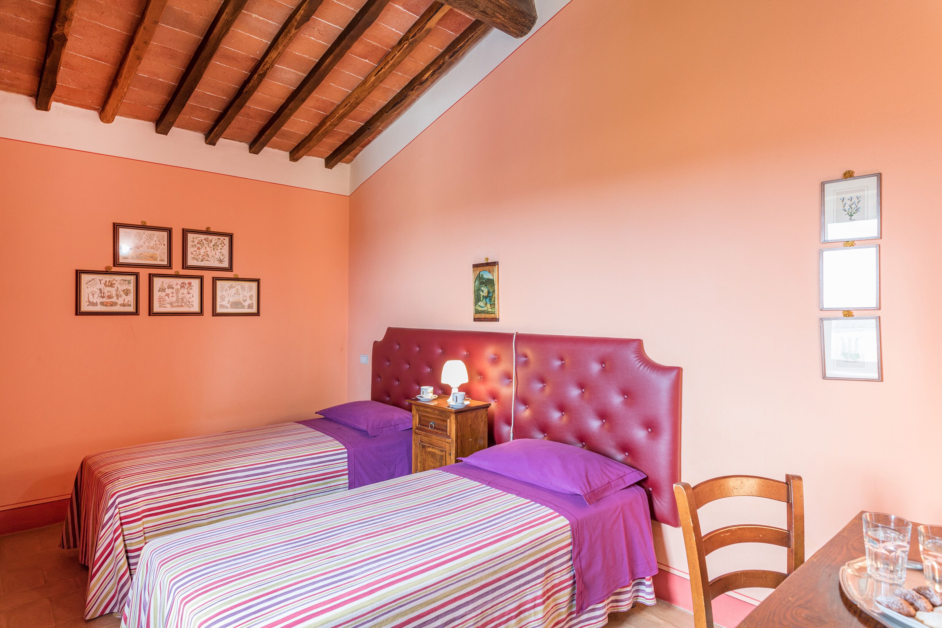 Una camera da letto con due letti, una testiera in legno, un comodino con una lampada e quadri appesi al muro.