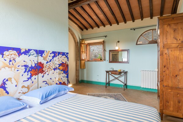 Un dormitorio con cama, armario de madera, ventana con cortinas, radiador y un mural floral en la pared.