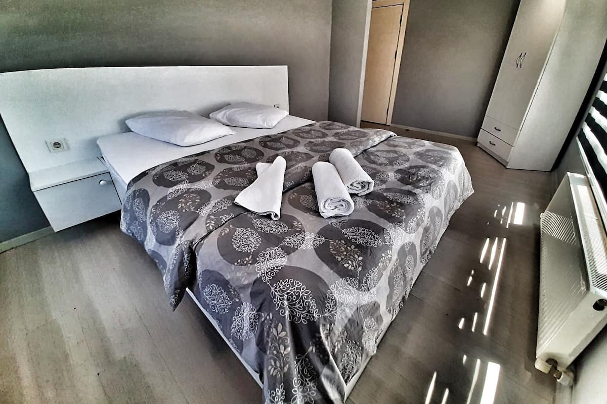 Una habitació d'hotel moderna amb un llit gran, una tauleta de nit, un armari i un radiador.