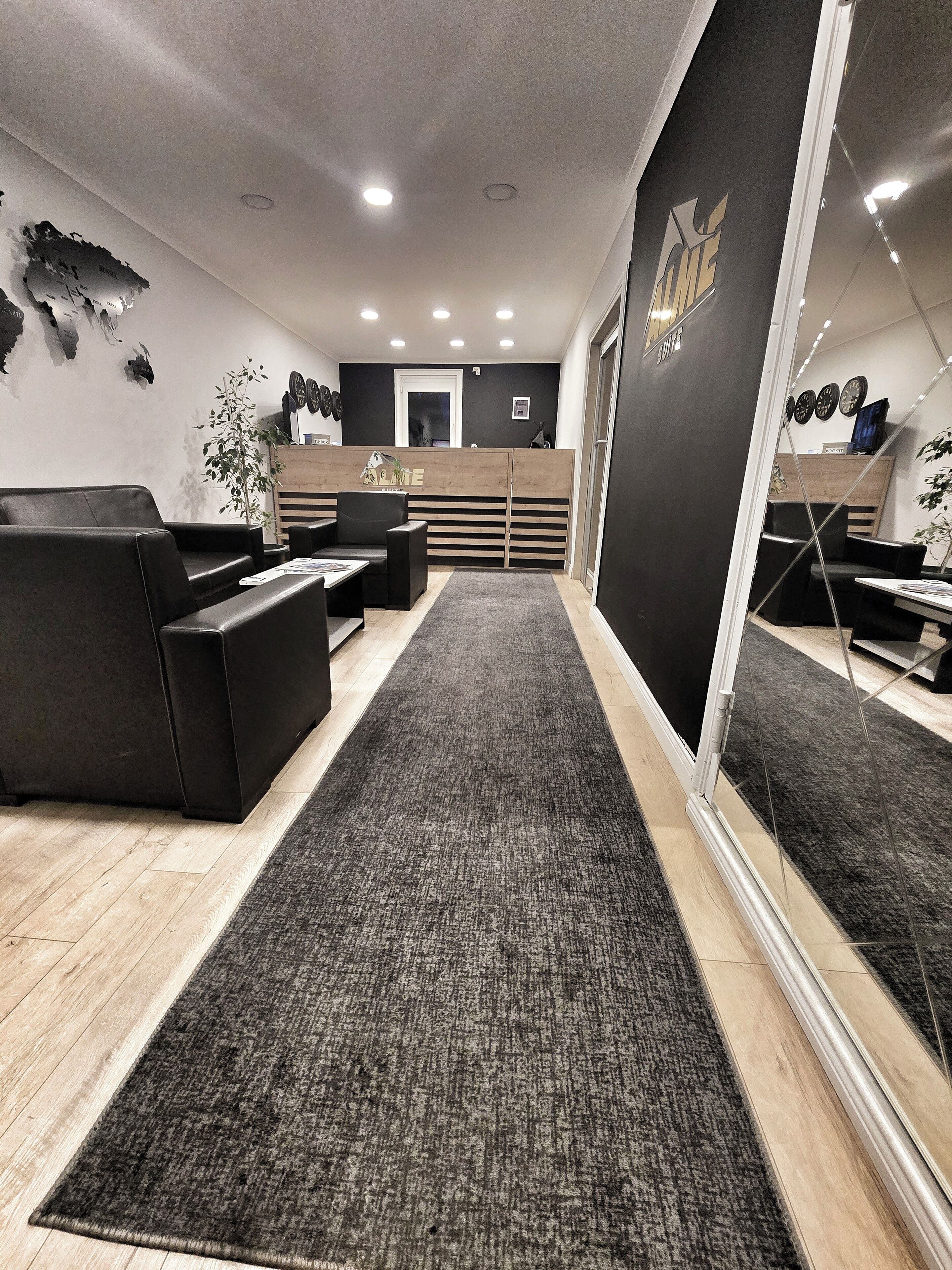 A reception area with a reception desk, black leather seating, a grey carpet, and a mirror reflecting the room.