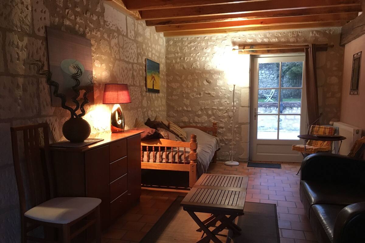 Ein gemütliches Zimmer mit Steinwand, Holzmöbeln, einem Bett, einem Tisch und einem Stuhl.
