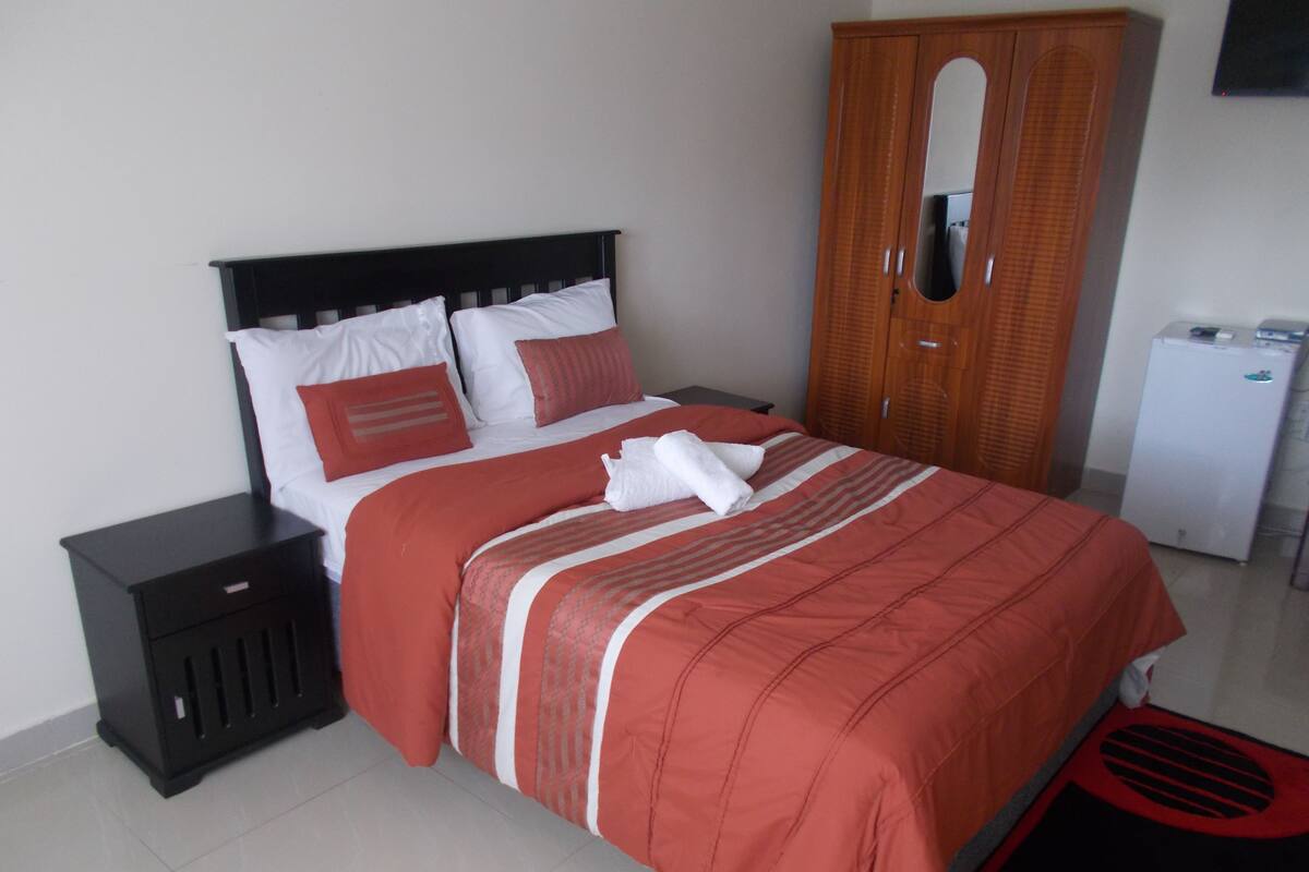 A neatly made bed with a red and white striped bedspread, a wooden headboard, and a white pillow.