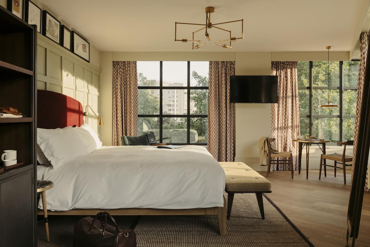 Ein Hotelzimmer mit einem großen Bett, einem Schreibtisch, einem Stuhl, einem Fernseher und einem Fenster mit Vorhängen.