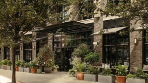 A modern building with a covered entrance, large windows, and potted plants along the walkway. - The Hoxton, Southwark (London)