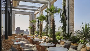 An outdoor seating area with wicker furniture, round tables, and potted plants. - The Hoxton, Southwark (London)