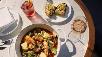 A seafood dish, a glass of red drink, and a plate with two pieces of bread on a table.