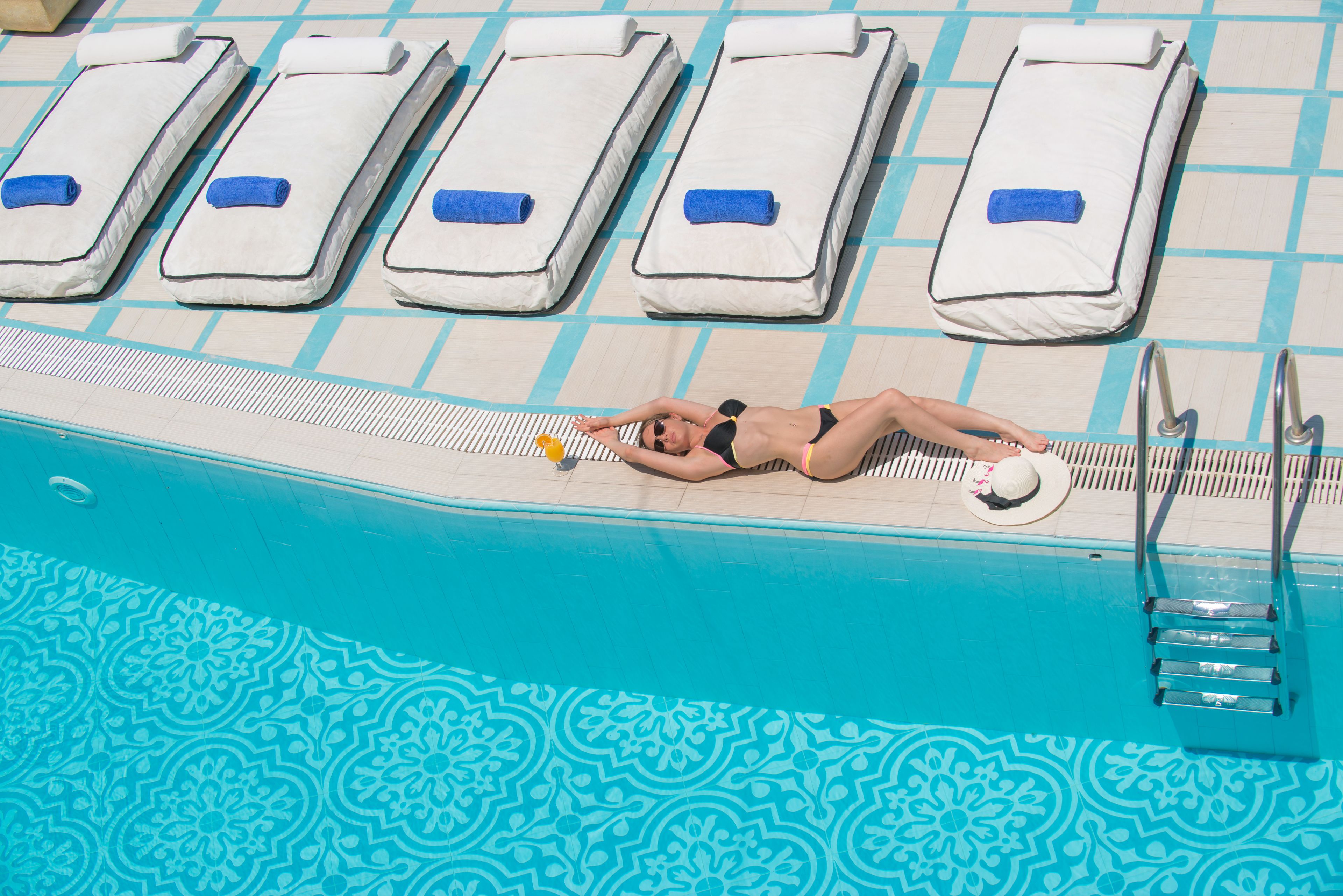 Uma área à beira da piscina com espreguiçadeiras e uma escada para entrar na piscina.