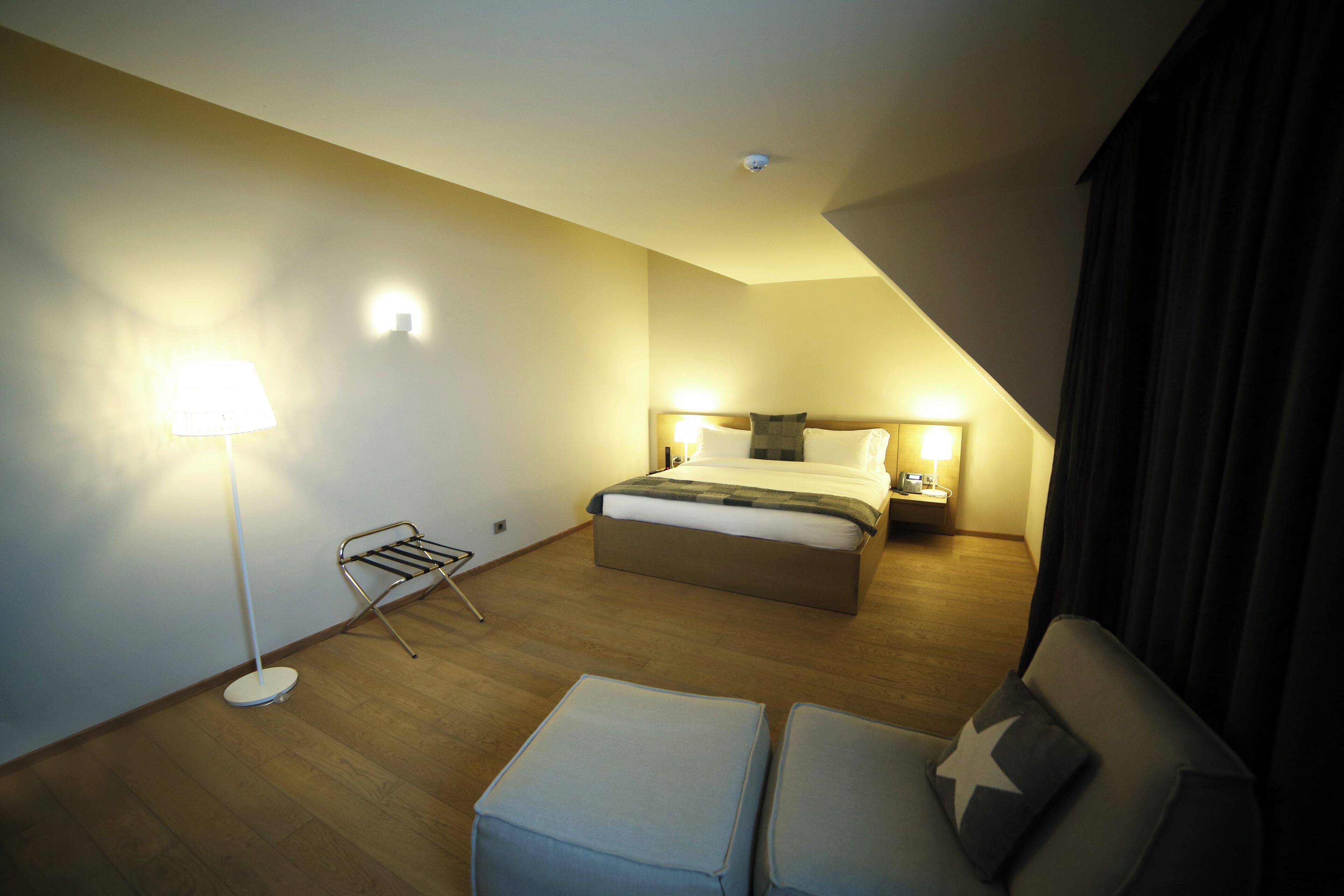 Una habitación de hotel moderna con cama, mesitas de noche, una lámpara de pie, un rincón de descanso con un cojín en forma de estrella y una cámara de seguridad instalada en el techo.