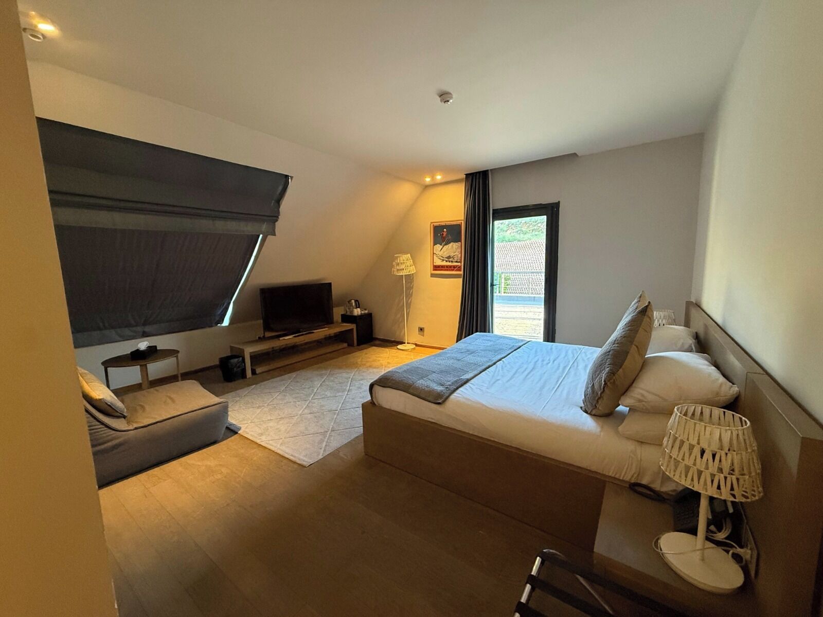A modern bedroom with a bed, a television, a small table, and a lamp.