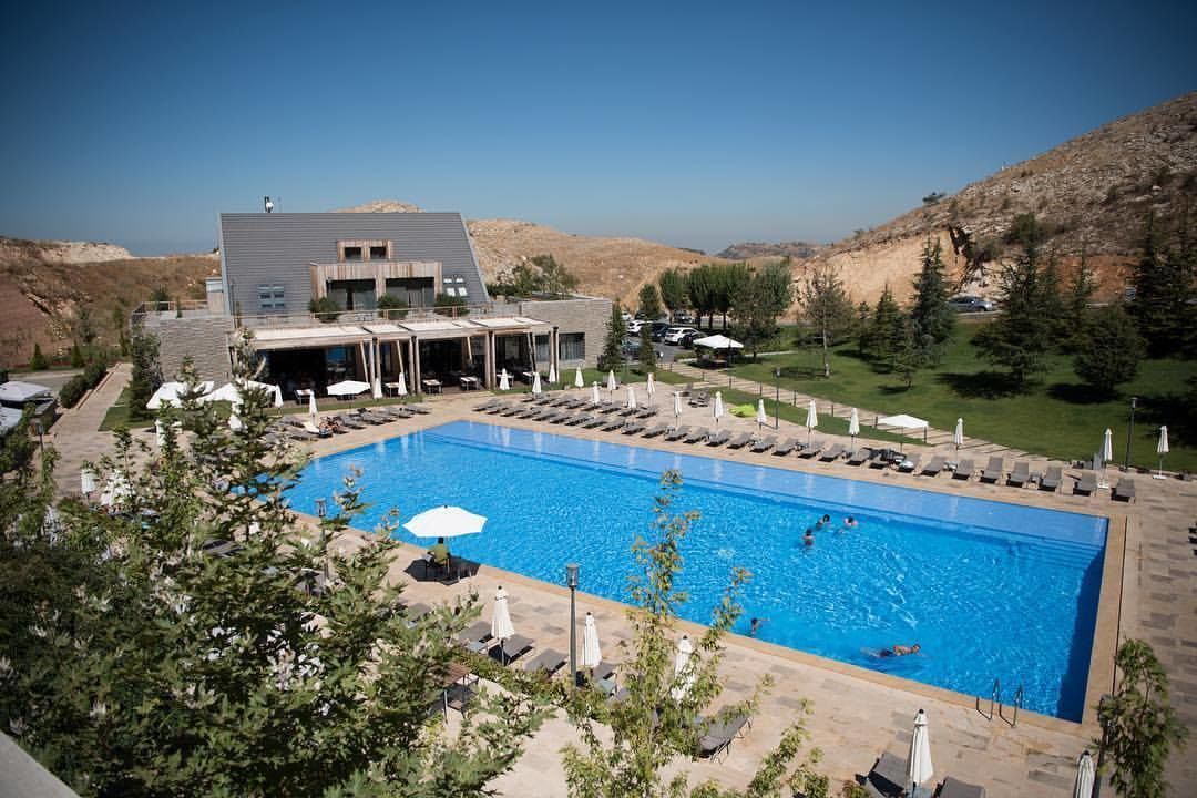 A modern hotel with a large swimming pool, outdoor seating, and a view of the surrounding hills.