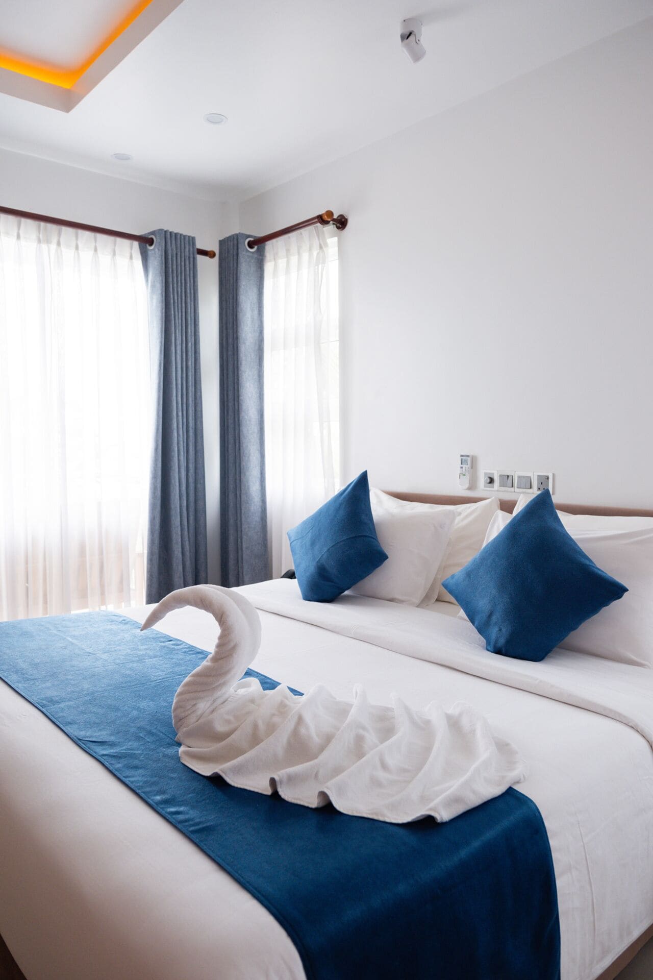 A hotel room with a bed, blue and white bedding, a white swan decoration, and a window with curtains.