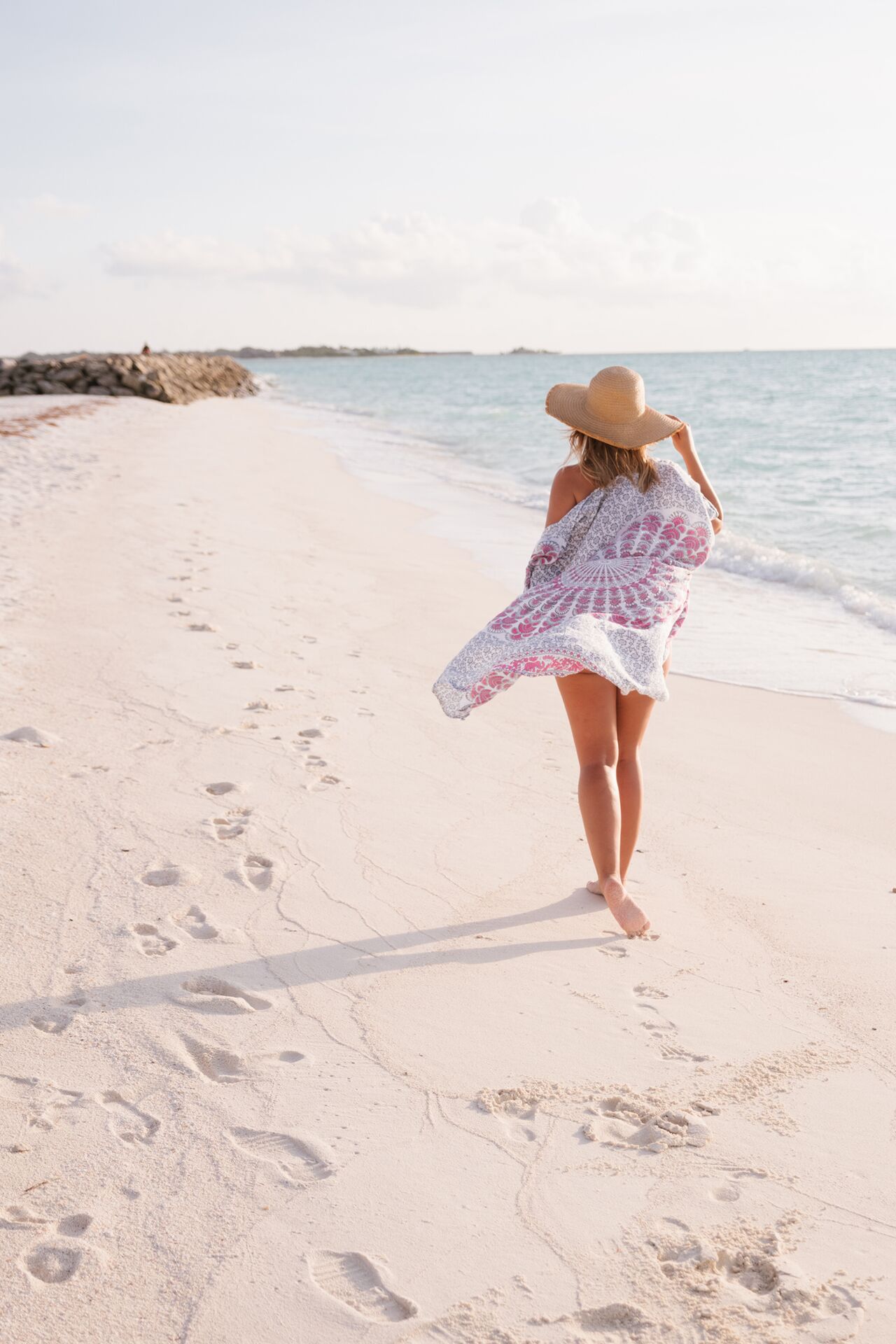 A person walking on a sandy beach with footprints leading towards the water.