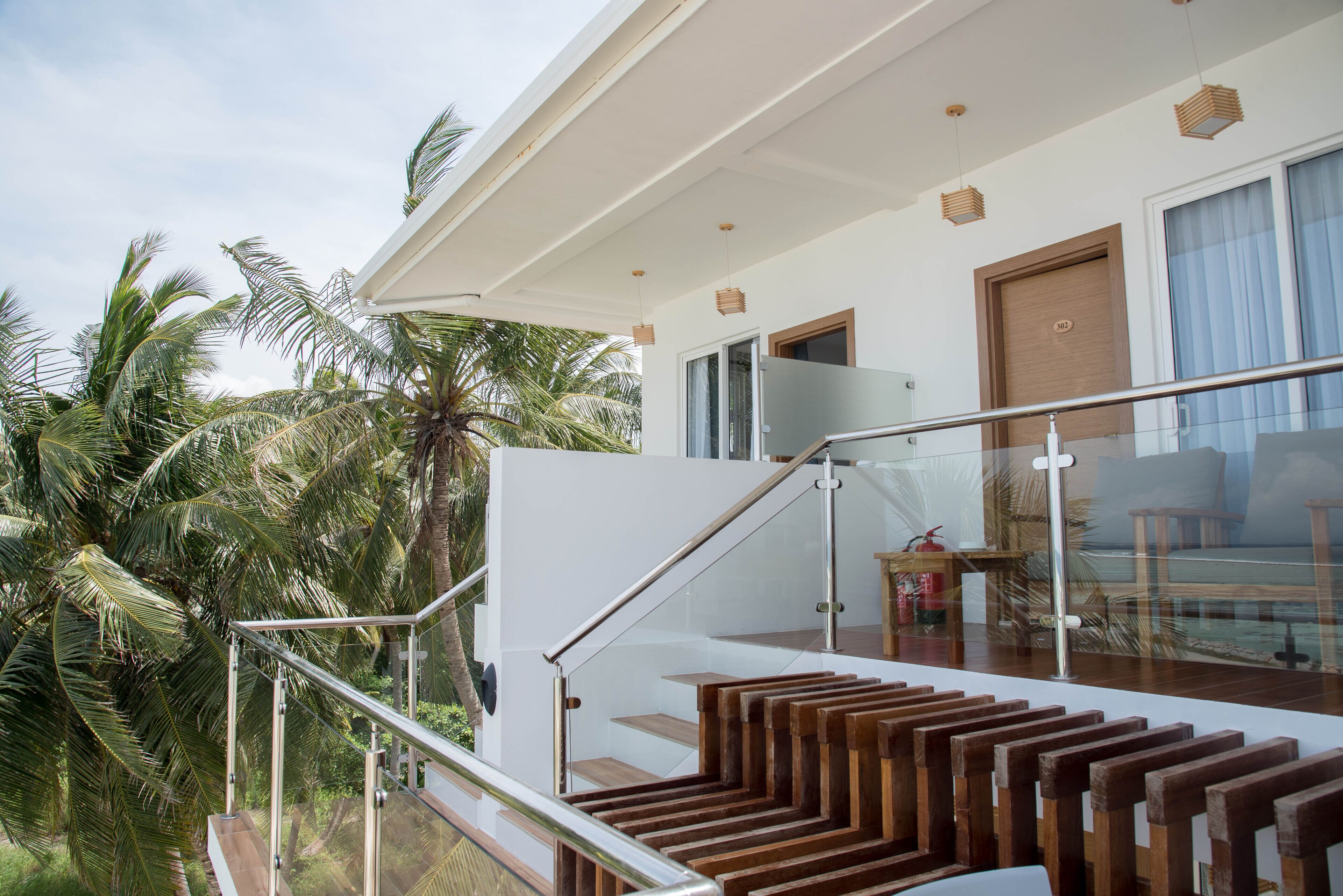Un hotel moderno con una escalera de cristal que da a un balcón, rodeado de palmeras.