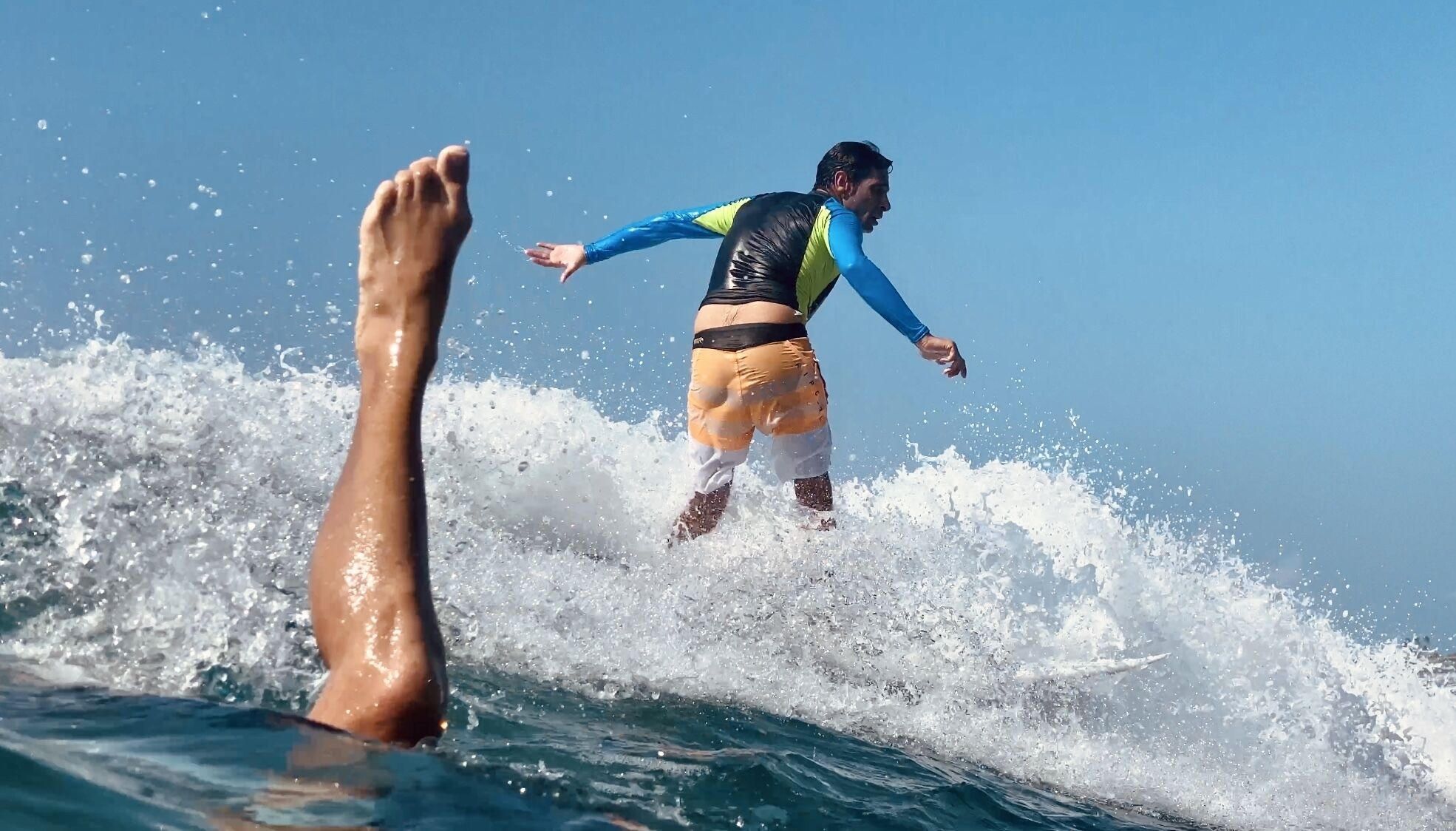 A person surfing on a wave with a clear blue sky in the background.