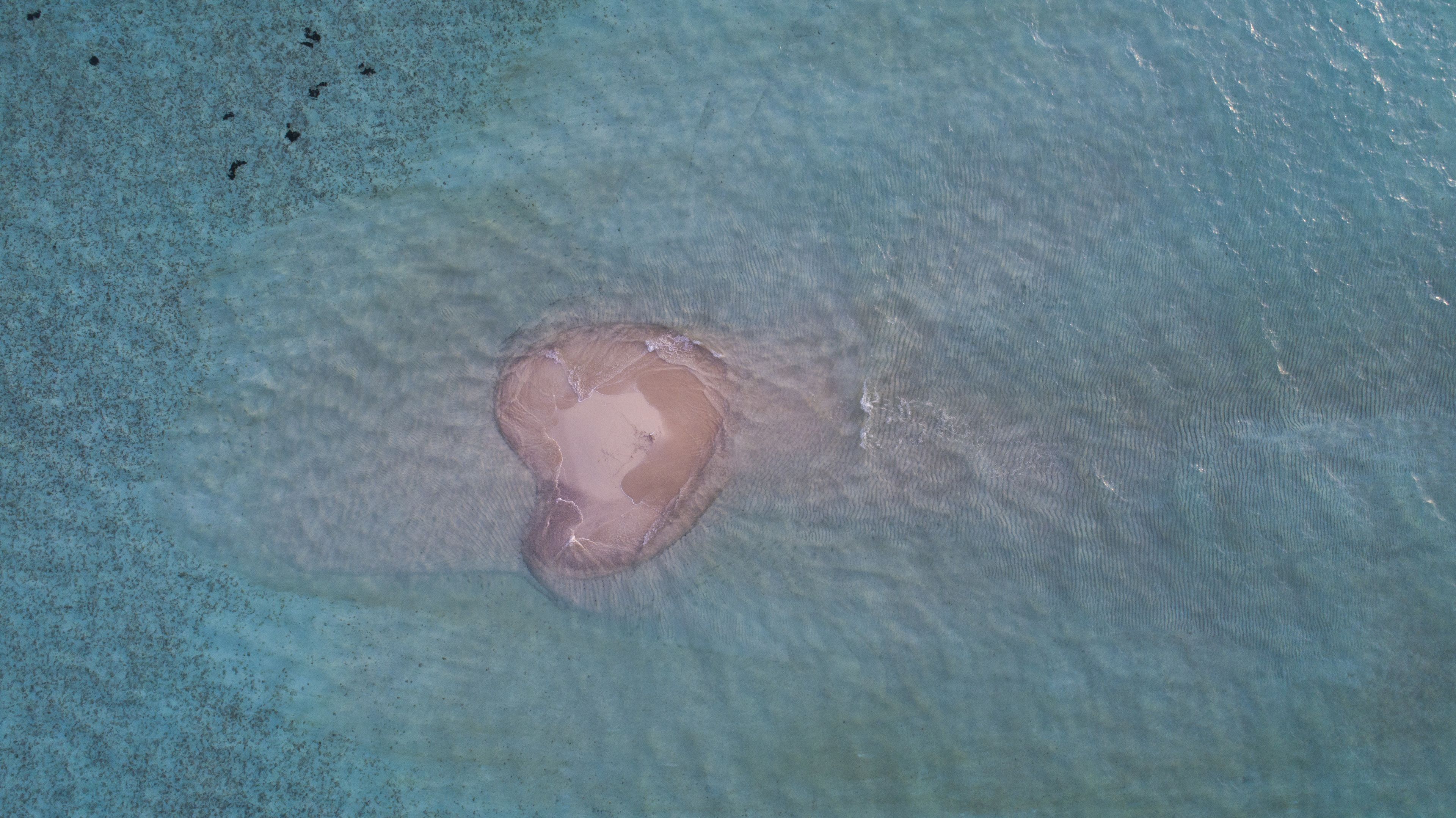 On peut clairement distinguer une plage avec une formation de sable en forme de cœur, entourée d’une eau calme.