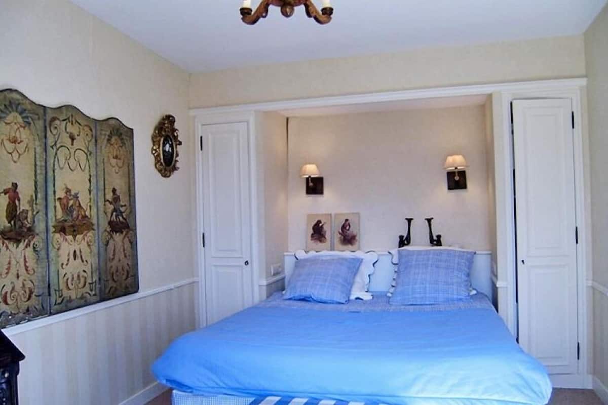 A bedroom with a large bed, two wall-mounted lamps, and a decorative panel on the wall.