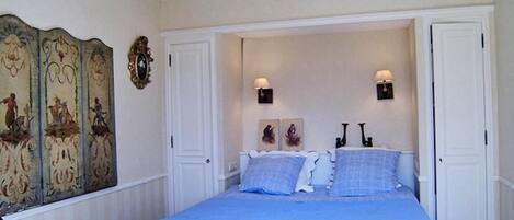 A bedroom with a large bed, two wall-mounted lamps, and a decorative panel on the wall.